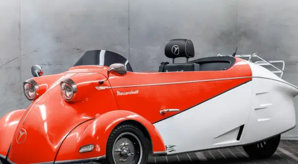 Ein leuchtend rotes und weißes Messerschmitt Auto mit Retro-Charme steht vor einer Betonwand.