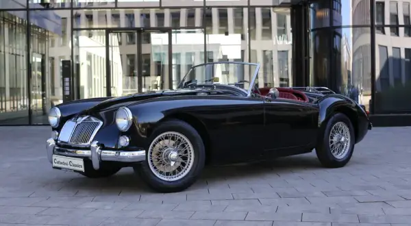 Schwarzer Roadster mit roten Ledersitzen, ein Klassiker unter den englischen Roadster Marken, steht vor einem modernen Gebäude.