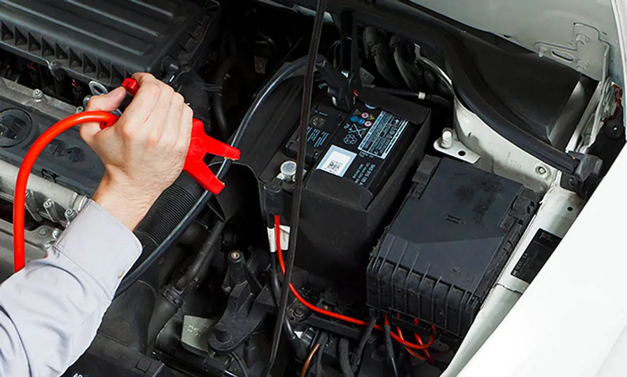 Hand klemmt rote Überbrückungsklemme an die Autobatterie, um sie zu laden.