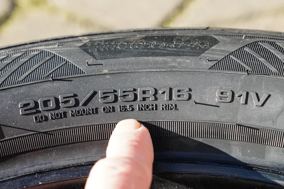 Ein Finger zeigt auf die Reifengröße 205/55R16, um die Zoll-Angabe abzulesen.
