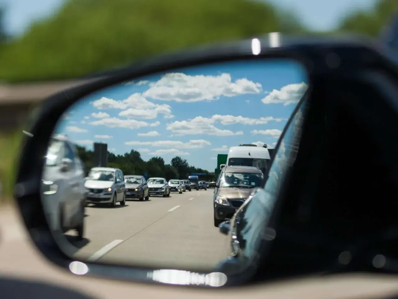 Autofahrer stellt den spiegel richtig ein, um den Verkehr auf der Autobahn zu sehen. Blauer Himmel mit Wolken spiegelt sich im Spiegel.