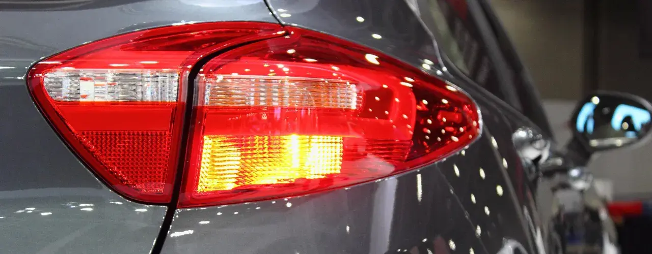 Rücklicht eines Autos, der Blinker blinkt schnell. Reflektionen auf dem grauen Lack.