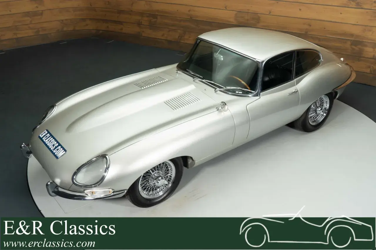 Silberner Jaguar E-Type Coupé mit Speichenrädern und Holzlenkrad, ein zeitloser Klassiker.