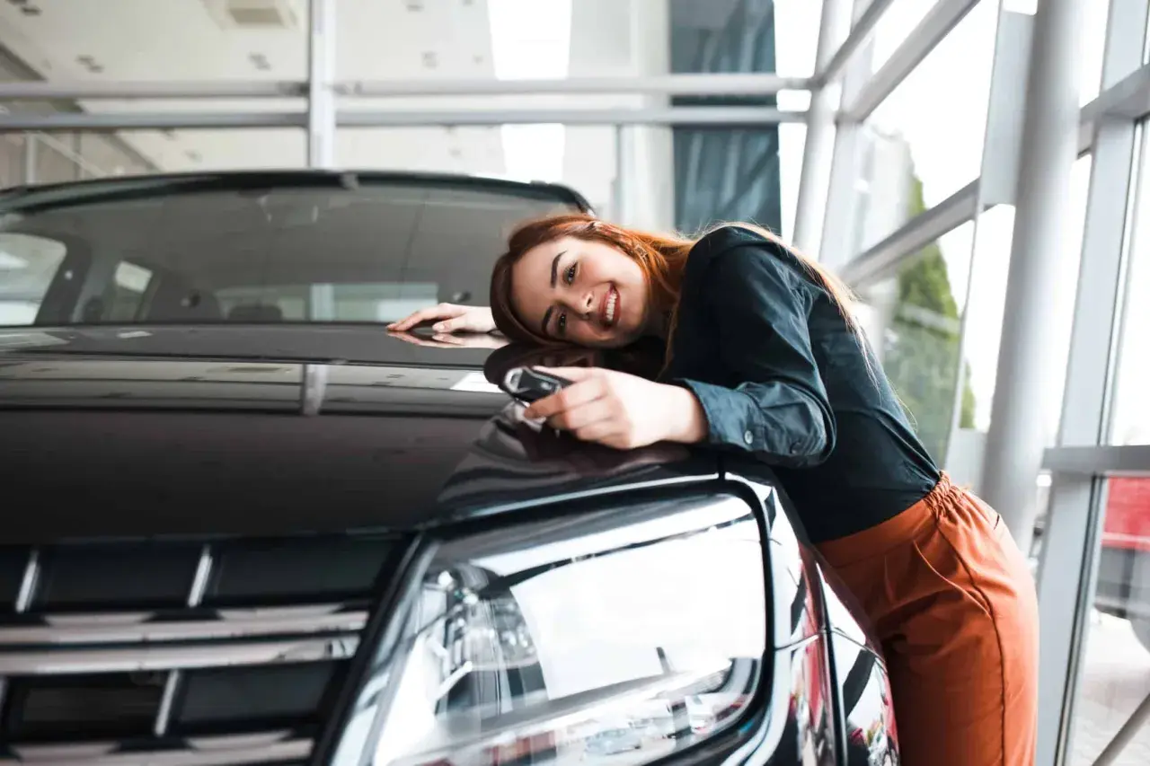 Glückliche Frau mit Autoschlüssel lehnt sich an ihren neuen Wagen. Der Traum vom Auto aus Belgien importieren wird wahr.