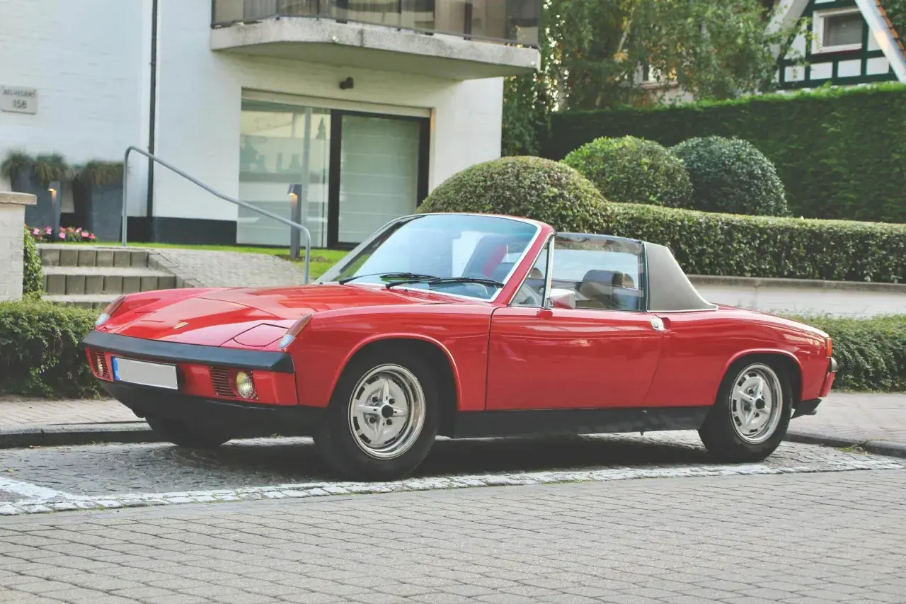 Roter Porsche 914 Roadster parkt vor einem modernen Haus mit gepflegten Hecken.