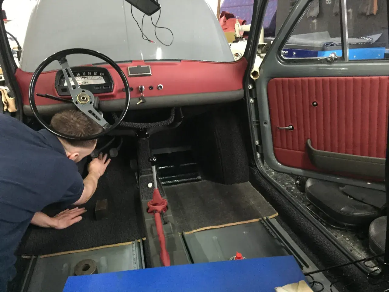 Der Mann arbeitet am fiat 500 oldtimer innenraum. Rote Türverkleidung und Armaturenbrett sind sichtbar.