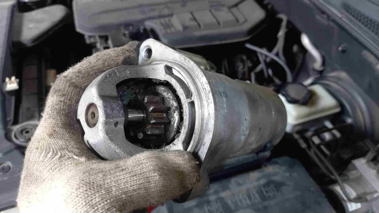 Defekter Anlasser Mercedes: Werkzeug in Handschuh hält ausgebauten Anlasser mit sichtbarem Ritzel. Kosten für Reparatur im Blick.
