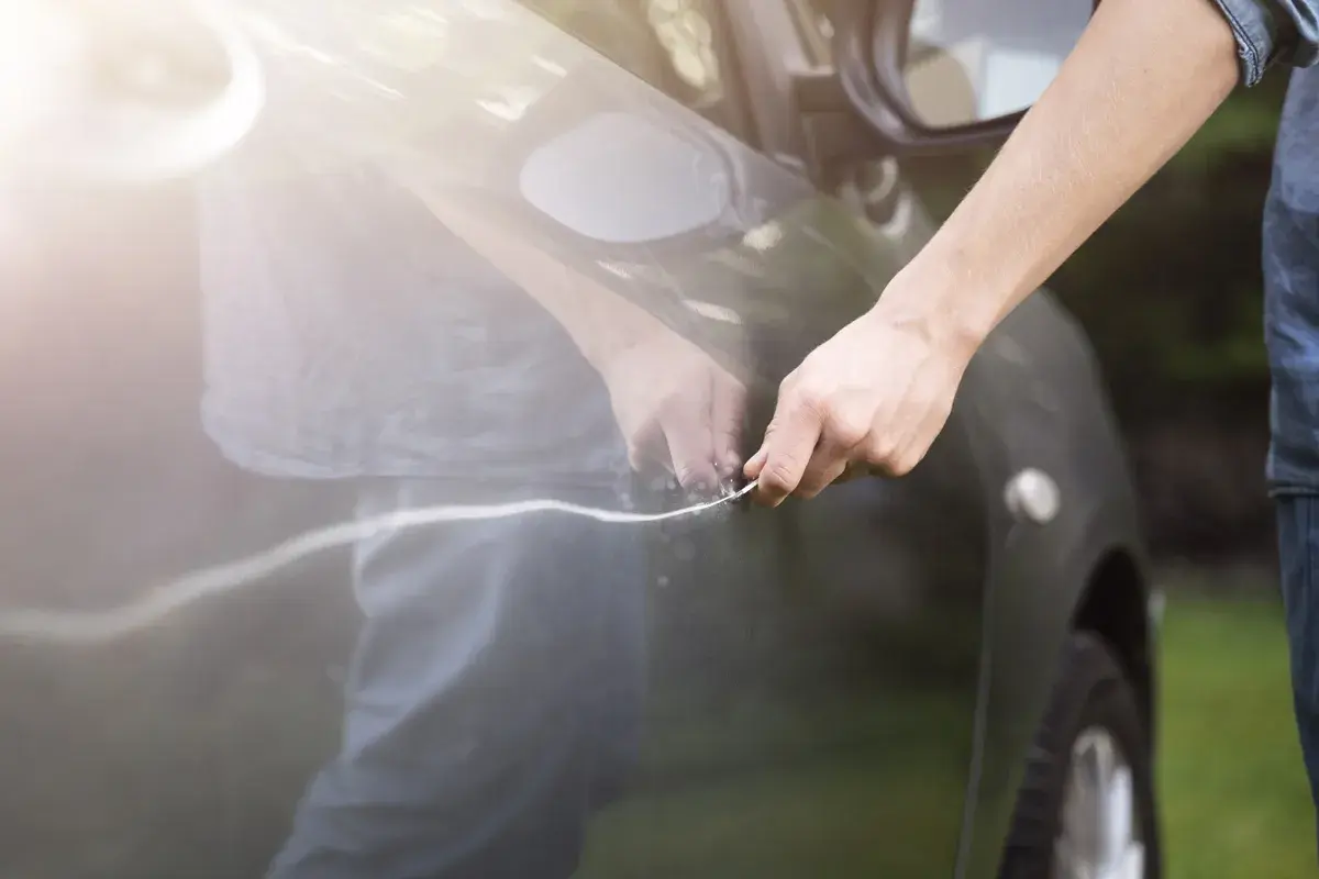 Person versucht, einen Kratzer am Auto mit einem Werkzeug auszubessern.
