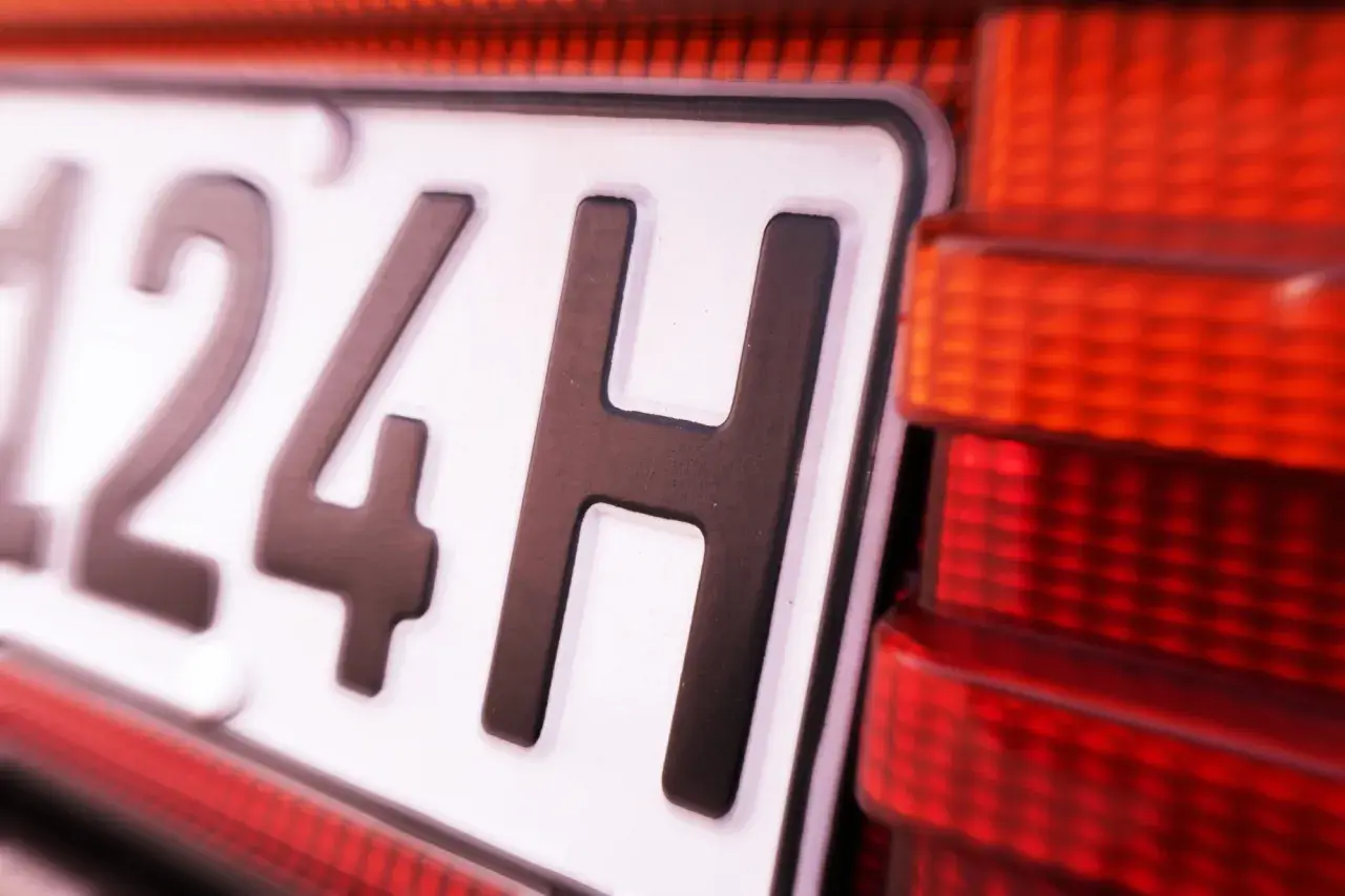 Nahaufnahme eines Nummernschilds mit der Aufschrift "124H". Daneben ist ein rotes Rücklicht zu sehen. Vielleicht eine Geschwindigkeitsbegrenzung?