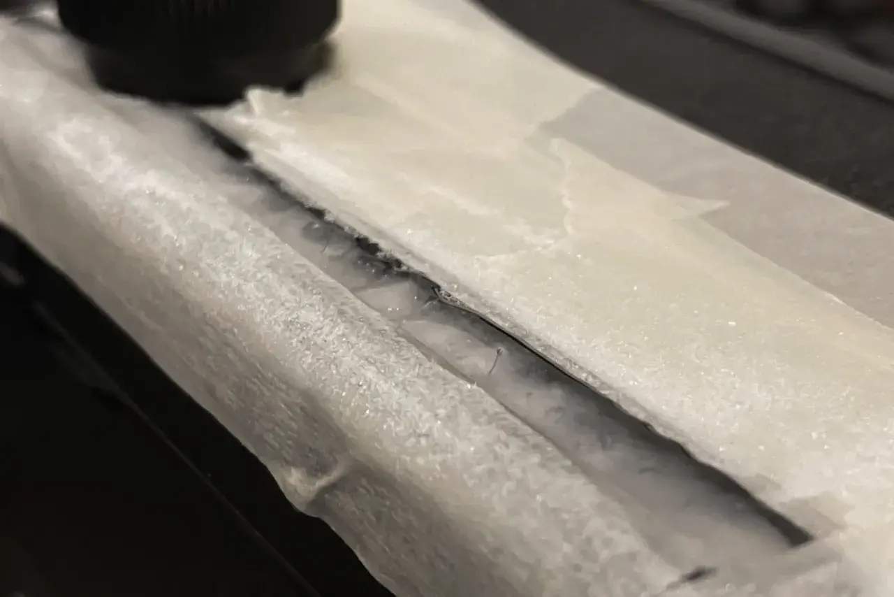Detailaufnahme: Riss in einem Bakelit-Teil, der mit Klebeband abgedeckt ist. Ein schwarzer Drehknopf ist im Hintergrund zu sehen. Hier wird Bakelit reparieren.
