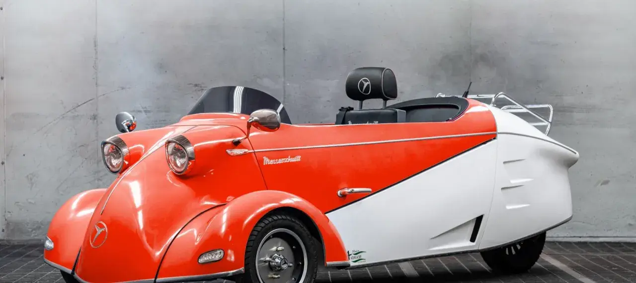 Ein leuchtend rotes und weißes Messerschmitt Auto mit Retro-Charme steht vor einer Betonwand.
