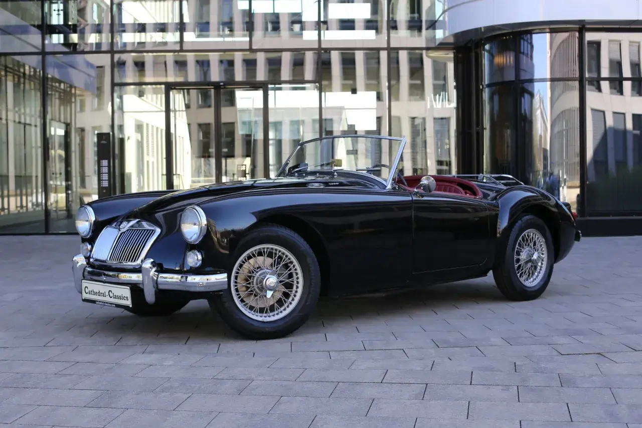Schwarzer Roadster mit roten Ledersitzen, ein Klassiker unter den englischen Roadster Marken, steht vor einem modernen Gebäude.