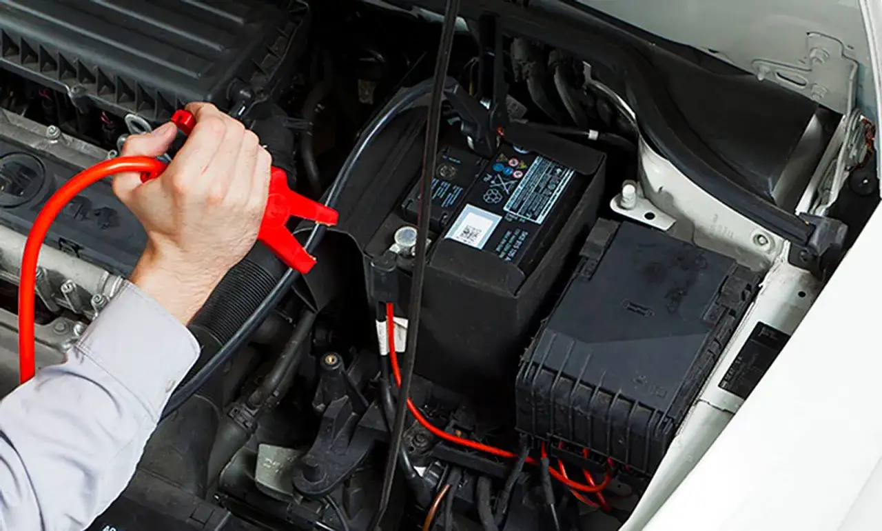 Hand klemmt rote Überbrückungsklemme an die Autobatterie, um sie zu laden.