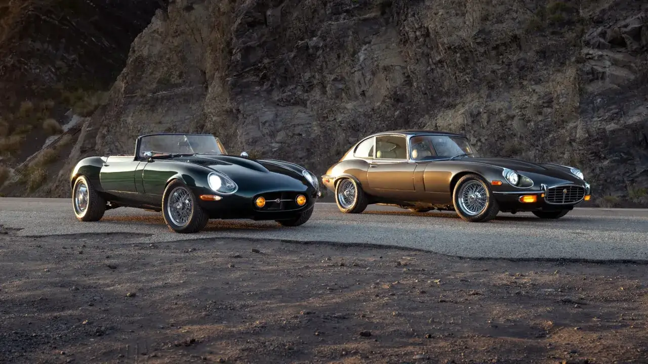 Zwei ikonische Jaguar E-Type Coup&eacute;s, ein gr&uuml;ner Roadster und ein bronzefarbener, stehen auf einer Stra&szlig;e vor einer Felswand.