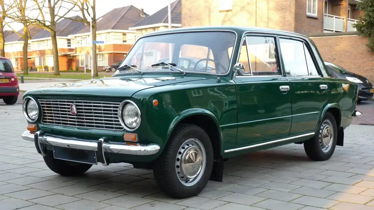 Gr&uuml;ner Lada Oldtimer parkt auf gepflastertem Weg vor H&auml;usern.