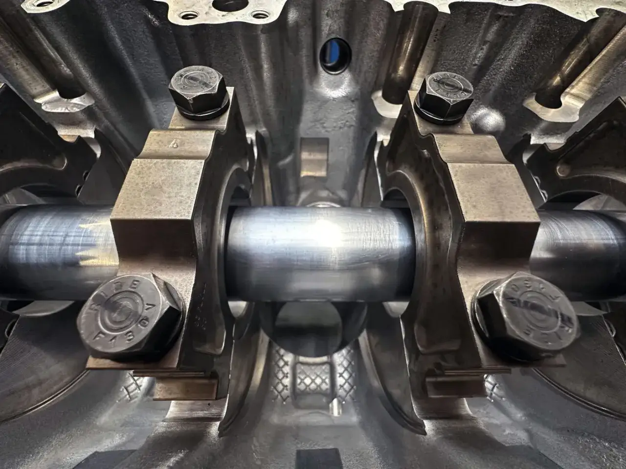 Detailaufnahme einer Kurbelwelle im Motorblock eines Autos. Die Lagerb&ouml;cke und Schrauben sind gut sichtbar.