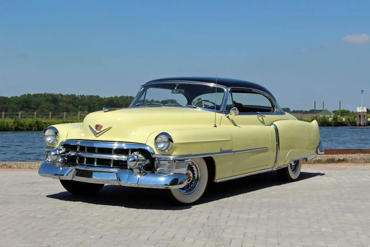 Ein gelber Cadillac Coup&eacute; mit schwarzem Dach steht am Wasser.