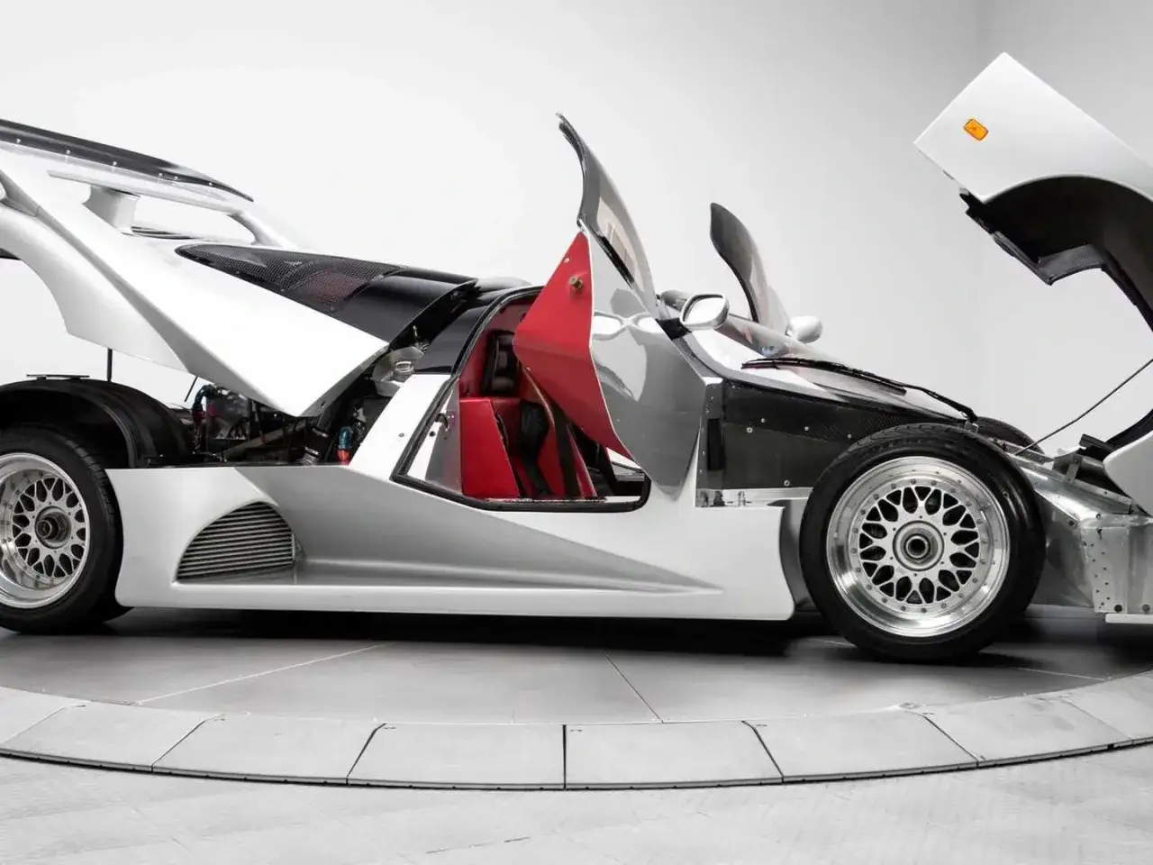 Silberner Lotec C1000 Supersportwagen mit ge&ouml;ffneten Fl&uuml;gelt&uuml;ren und Motorhaube. Rote Ledersitze sind sichtbar.
