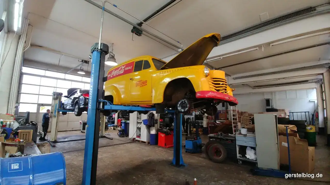 Gelber Oldtimer mit Coca-Cola-Werbung auf Hebeb&uuml;hne, bereit f&uuml;r die Oldtimer Restauration.