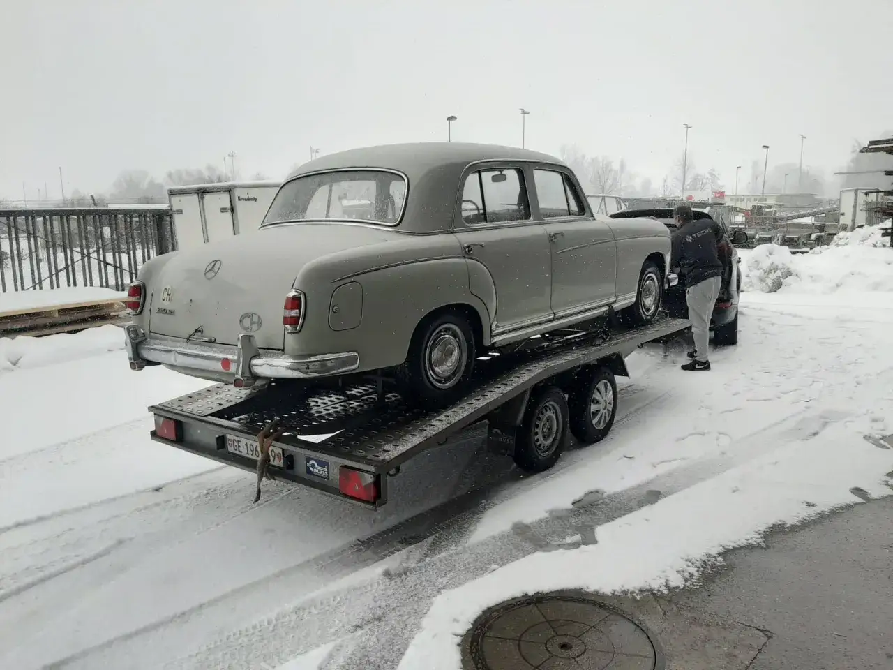 Ein grauer Mercedes Ponton wird im Schnee auf einen Anh&auml;nger geladen.