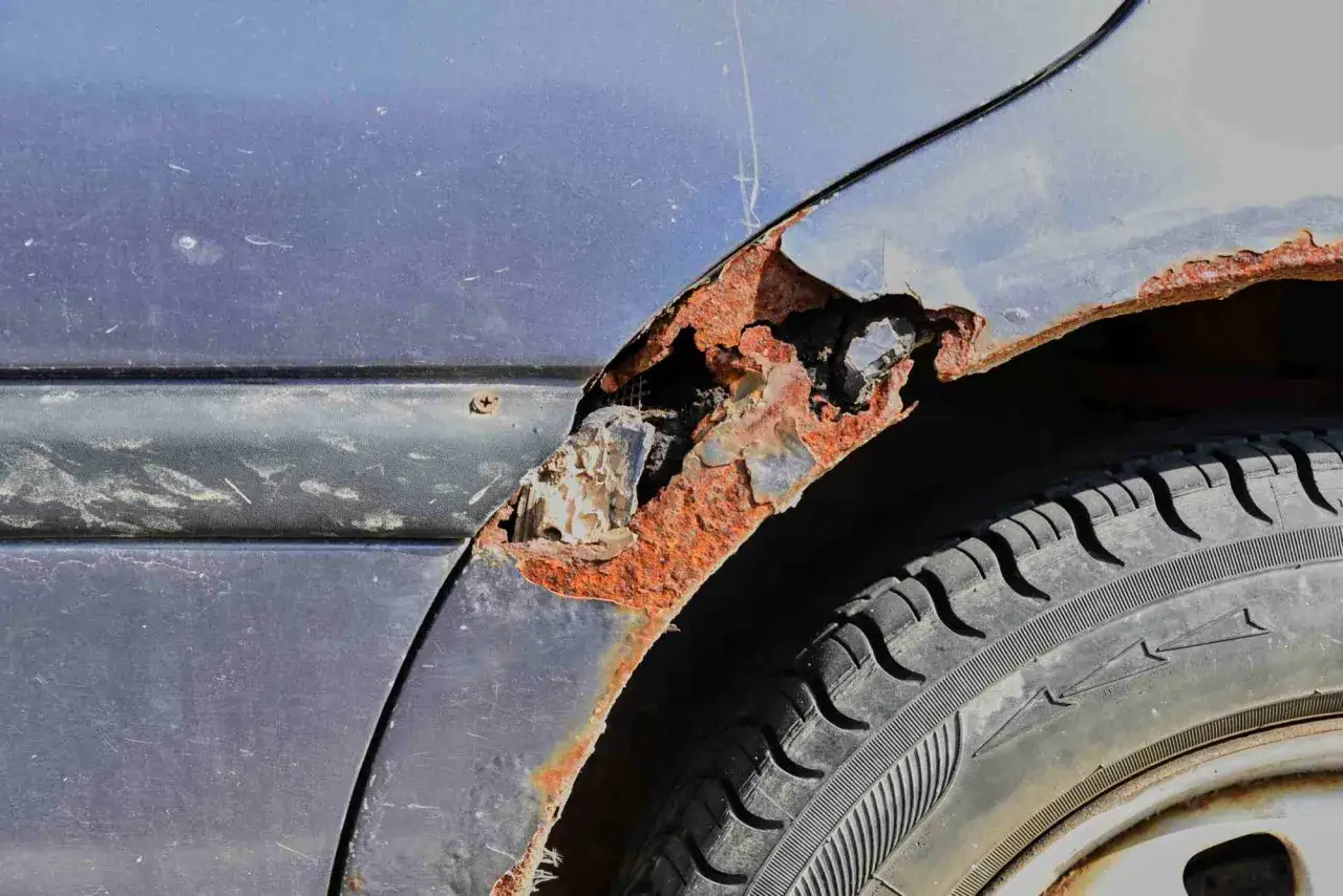 Starker Rost unter dem Lack am Kotflügel eines Autos. Die Rostschicht ist dick und bröckelt ab, was zeigt, wie wichtig es ist, Rost unter Lack zu entfernen, bevor er das Metall zerstört.