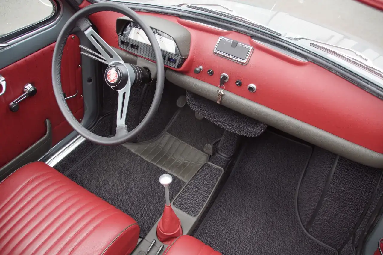 Der Innenraum eines Fiat 500 Oldtimers mit roten Ledersitzen und Armaturenbrett. Das Lenkrad und der Schalthebel sind gut sichtbar.