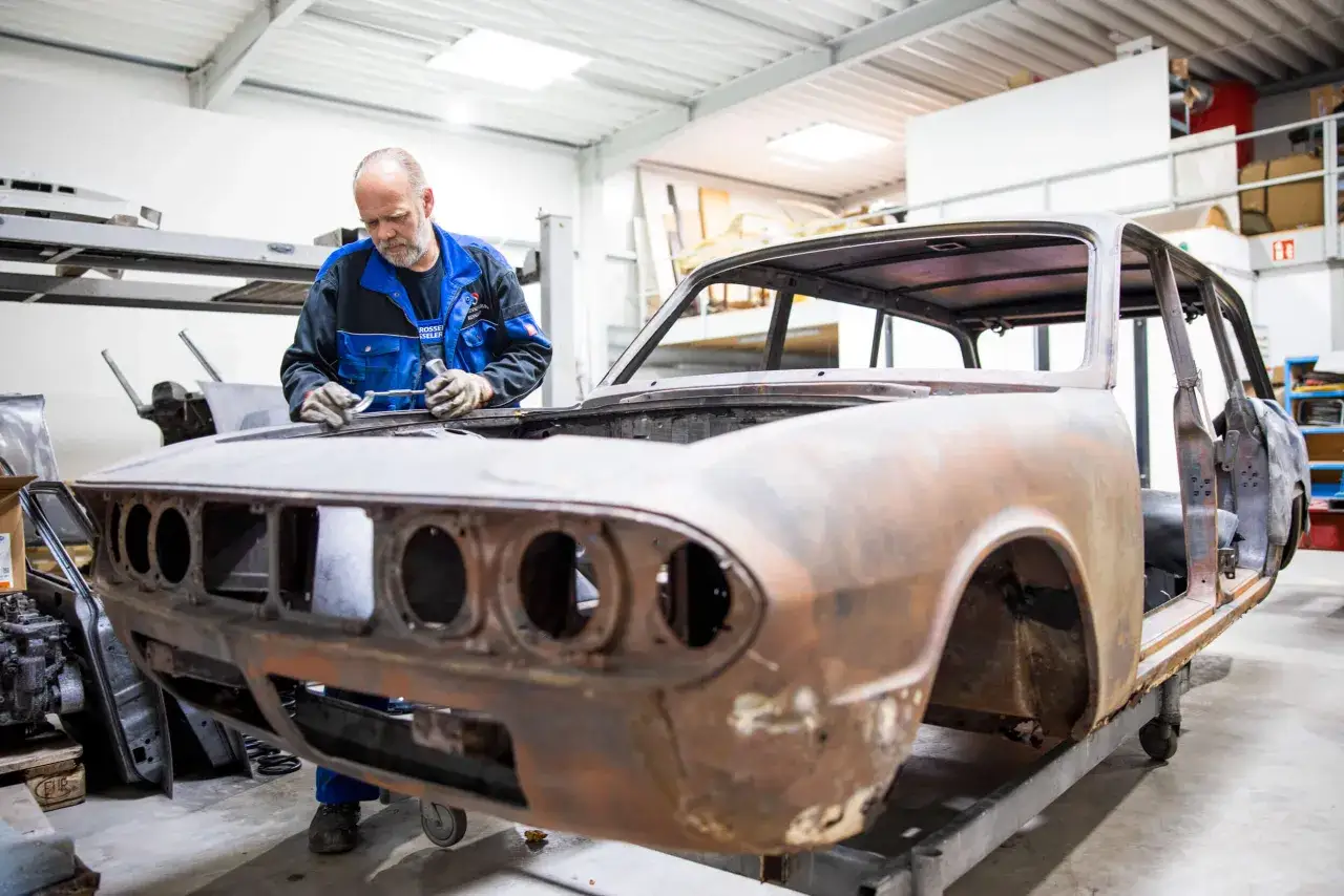 Mann arbeitet an rostiger Oldtimer-Karosserie. Die Kosten f&uuml;r das Oldtimer lackieren sind hoch, aber die Restaurierung lohnt sich.
