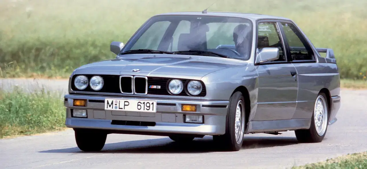 Silberner BMW E30 M3, Baujahr 1986, fährt auf einer Landstraße.