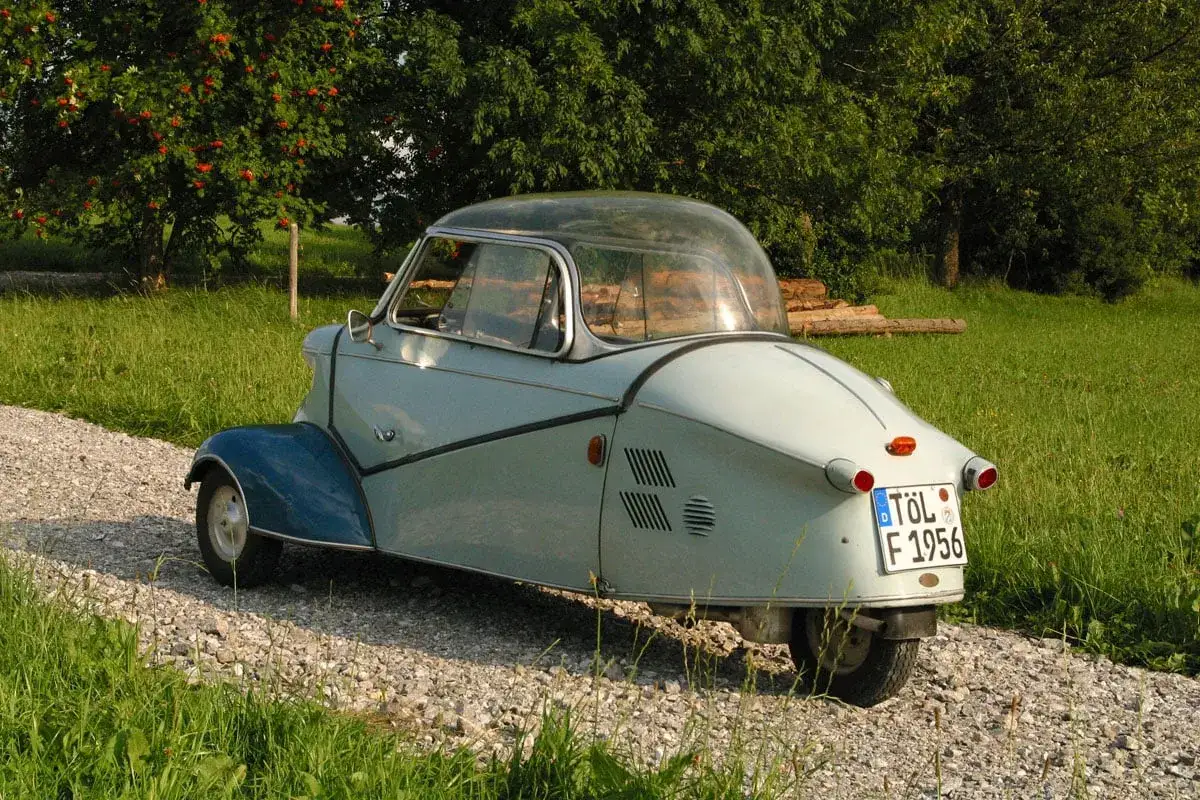Ein hellblaues Messerschmitt Auto mit Glaskuppel f&auml;hrt auf einem Schotterweg durch gr&uuml;nes Gras.