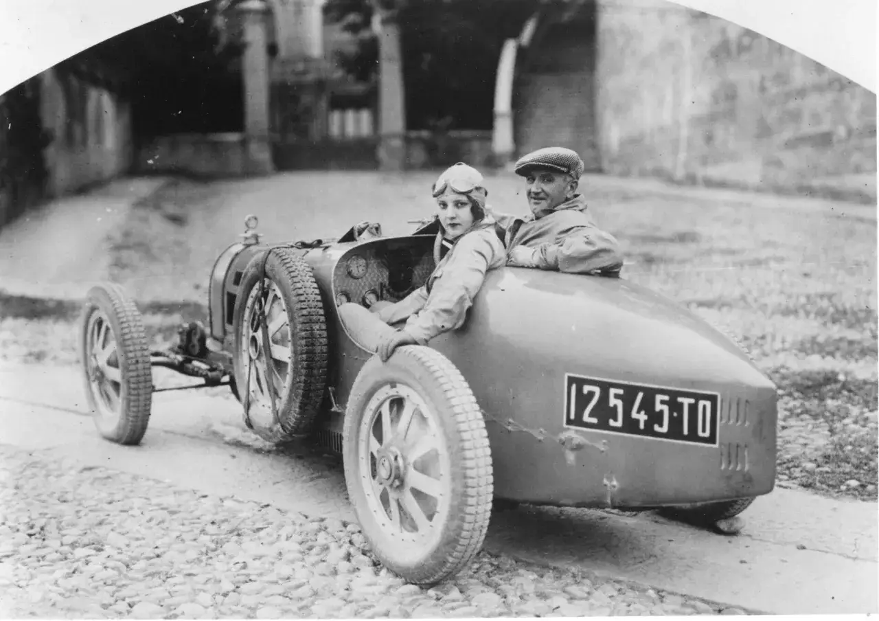 Ein Mann und eine Frau in Rennkleidung sitzen in einem Bugatti Type 35.