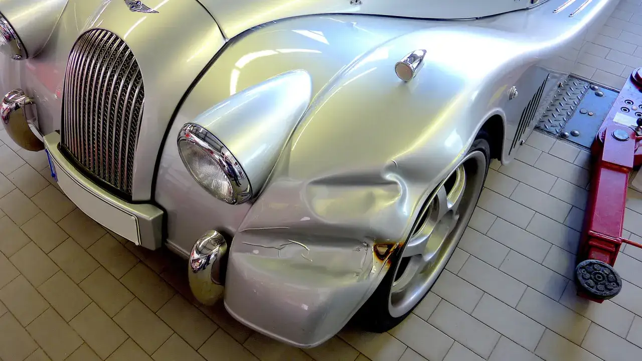 Silberner Oldtimer mit deutlichen Dellen und Rostsch&auml;den am Kotfl&uuml;gel, bereit f&uuml;r eine Frame-off-Restaurierung.