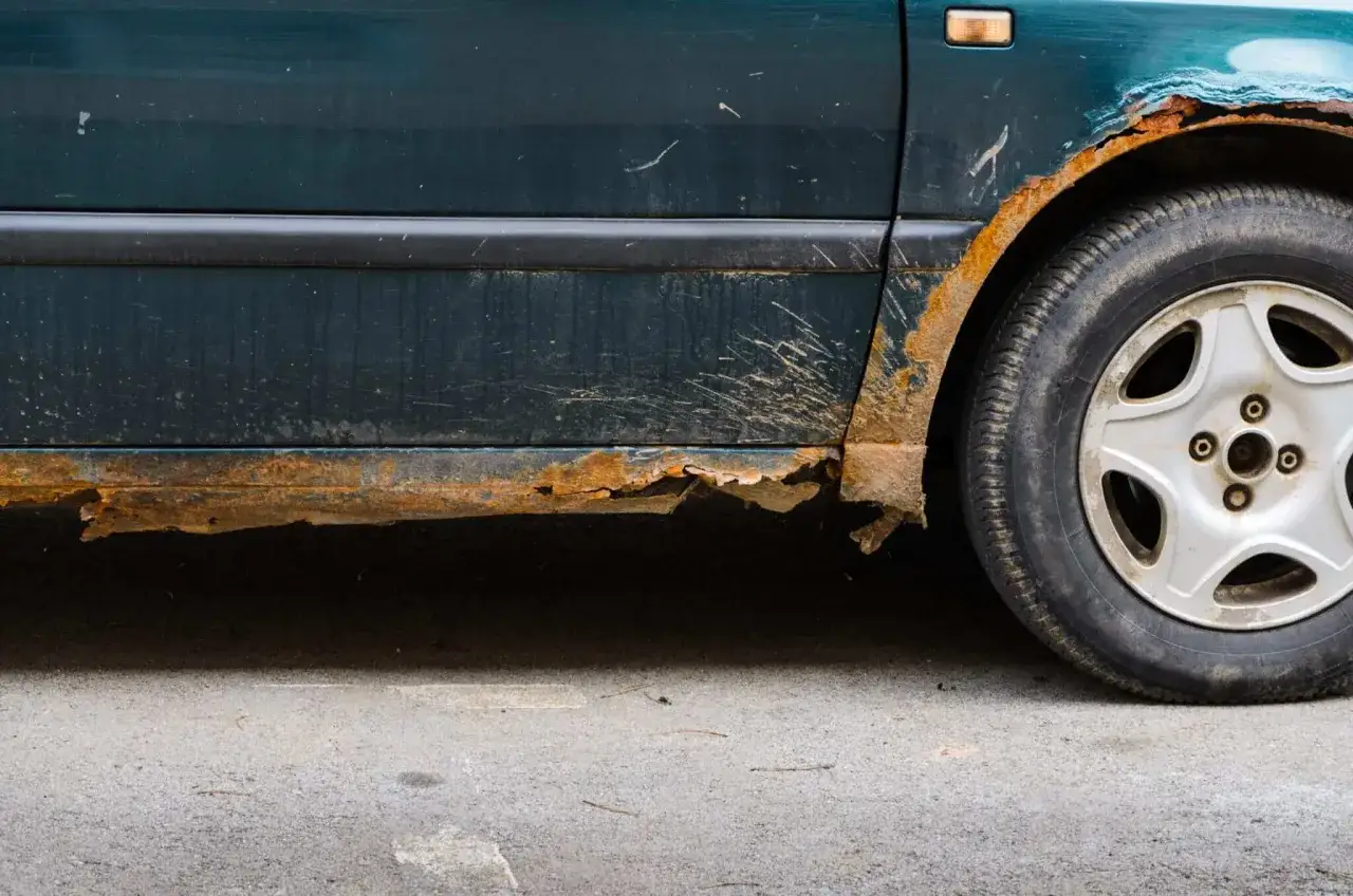 Stark verrosteter Schweller eines Autos, der dringend auto entrosten ben&ouml;tigt. Rostige Blechteile br&ouml;ckeln ab.