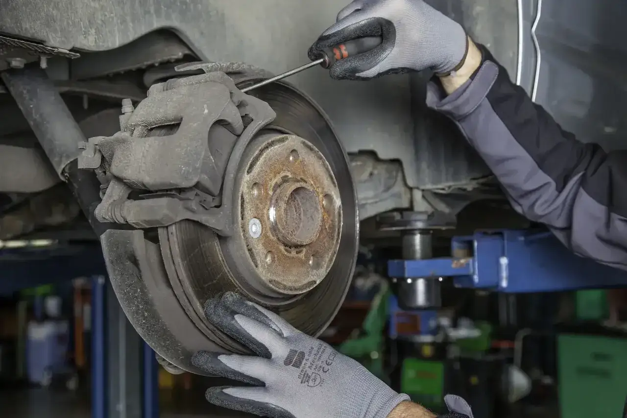 Mechaniker mit Handschuhen prüft Bremsscheiben. Ein Schraubenzieher wird benutzt, um zu sehen, wann bremsscheiben wechseln nötig ist.