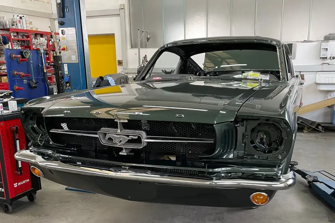 Dunkelgrüner Oldtimer, ein Ford Mustang, in der Werkstatt. Die Scheinwerfer fehlen, was auf eine laufende oldtimer restauration kosten hinweist.