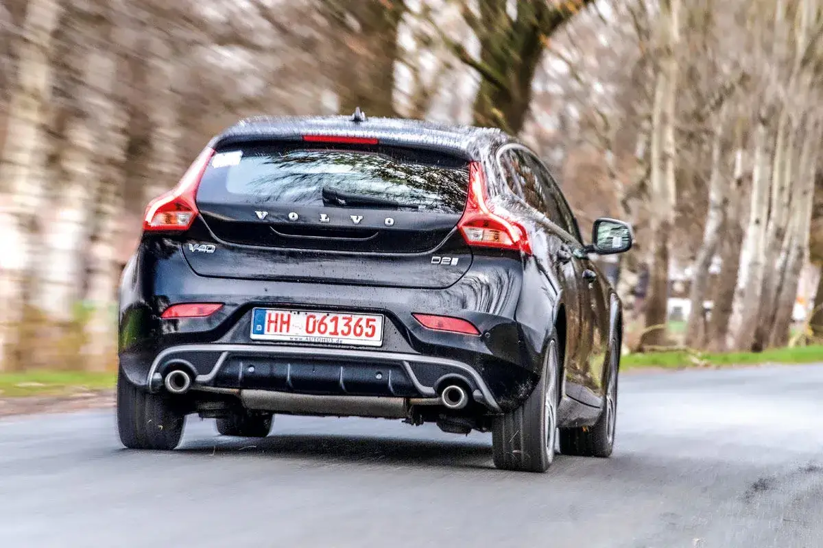 Schwarzer Volvo V40 f&auml;hrt auf einer Stra&szlig;e, umgeben von B&auml;umen.