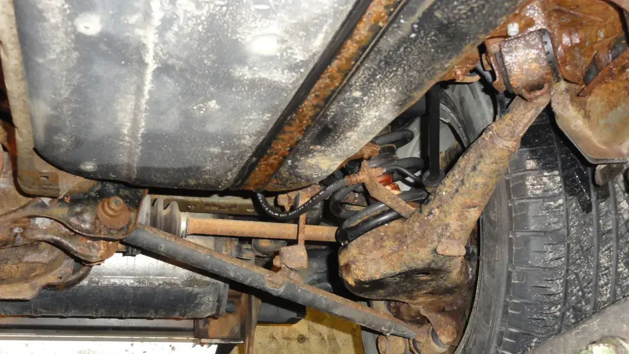Stark verrostete Achsteile und ein Tank erfordern dringend unterboden entrosten. Rostige Metallteile und eine Feder sind sichtbar.