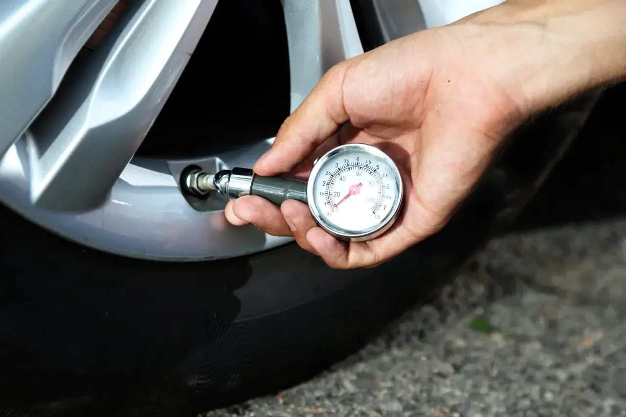 Hand prüft mit Manometer den Reifendruck des Autos. Der Zeiger zeigt einen Wert um 2,5 bar an.