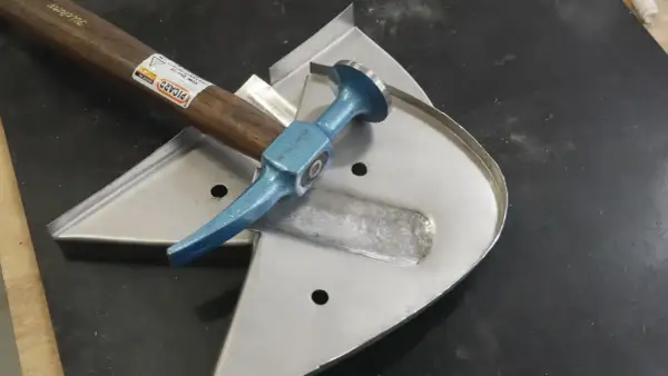 Karosserie Werkzeug für Oldtimer: Ein Ausbeul-Pinnhammer liegt auf einem Blechteil, bereit für die Restaurierung.