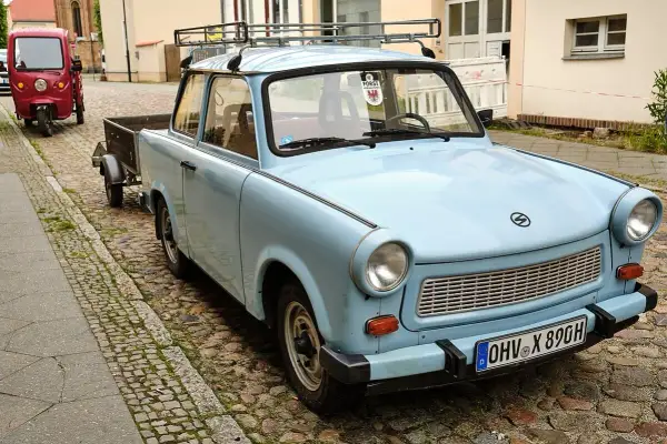 Hellblauer Trabant Kübelwagen mit Anhänger, Baujahr und Zulassung erkennbar.