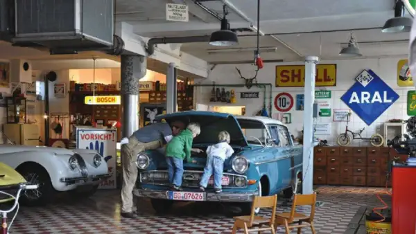 Familie bei der Oldtimer-Restauration eines blauen Opels. Der Vater erklärt den Kindern den Motorraum.