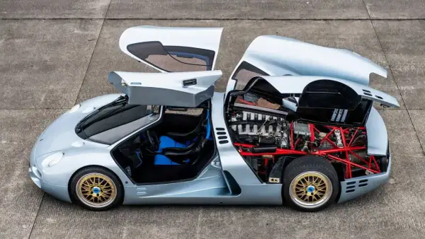 Der Isdera Commendatore 112i mit geöffneten Flügeltüren und Motorhaube zeigt seinen V12-Motor und die rote Gitterrohrrahmen-Konstruktion.