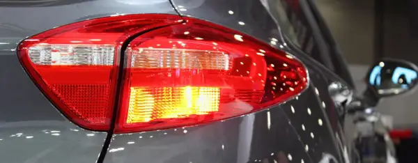 Rücklicht eines Autos, der Blinker blinkt schnell. Reflektionen auf dem grauen Lack.