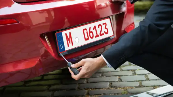 Mann schraubt Kennzeichen an rotes Auto. So bekommt man ein rotes Kennzeichen für Überführungsfahrten.