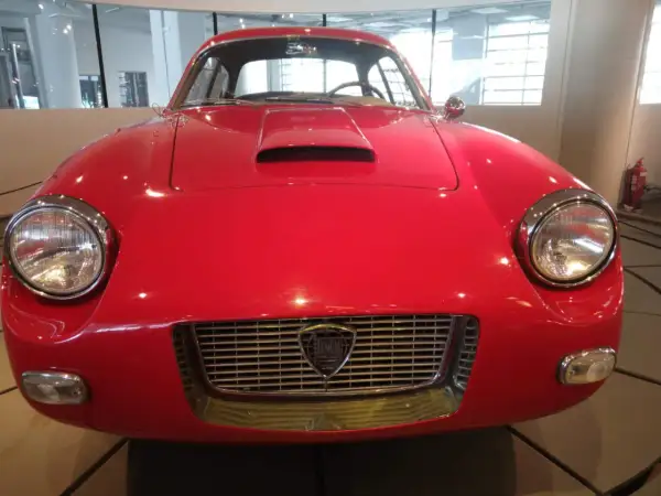 Vorderansicht eines roten italienischen Oldtimers mit Lancia-Logo im Kühlergrill.
