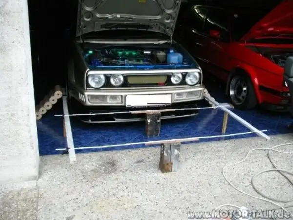 Selbstgemachte Achsvermessung: Ein silberner VW Golf mit geöffneter Haube steht bereit. Daneben ein roter Wagen.