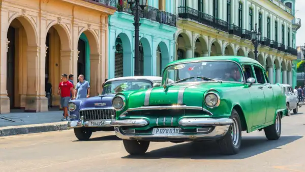 Grüne und blaue Oldtimer fahren auf einer Straße in Havanna. Diese Autos sind ein Symbol für die Geschichte und den Charme der Stadt, die man oft bei einem **oldtimer importieren** erleben kann.