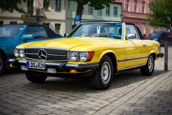 Ein leuchtend gelber Mercedes-Benz SL Roadster, ein Klassiker unter den retro autos, parkt auf einem Kopfsteinpflasterplatz.