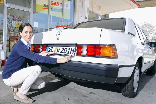 Frau befestigt ein H-Kennzeichen an einem weißen Mercedes. Was kostet ein H Kennzeichen?