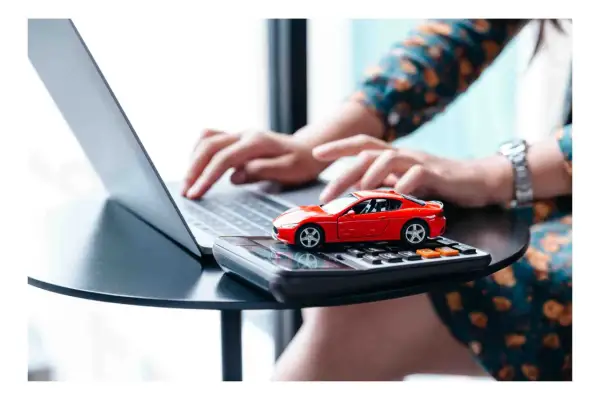 Rote Spielzeugauto auf Taschenrechner, während Hände auf Laptop tippen. Möglicherweise Vorbereitung für die auto abmelden.