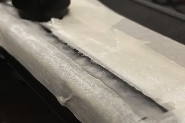 Detailaufnahme: Riss in einem Bakelit-Teil, der mit Klebeband abgedeckt ist. Ein schwarzer Drehknopf ist im Hintergrund zu sehen. Hier wird Bakelit reparieren.